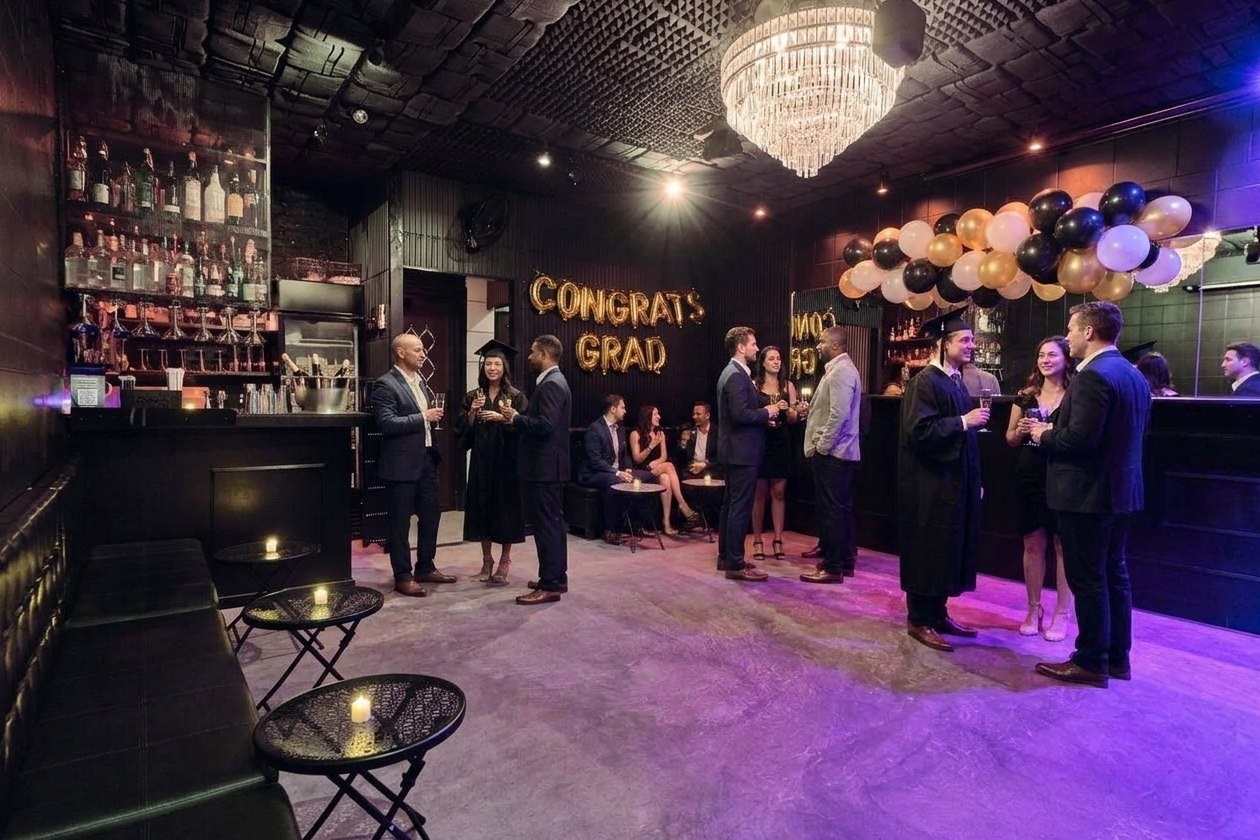 Styled illustration: the Back Room at B Lounge NYC dressed for a graduation party, with black and gold balloons and a Congrats Grad banner